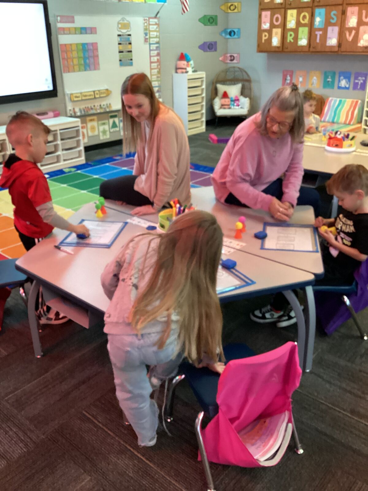 Children and adults engage in an activity at tables in a classroom setting.