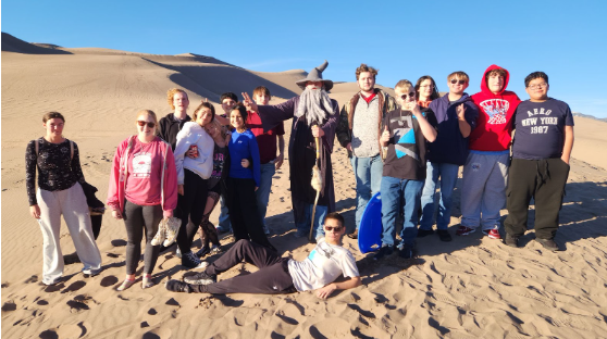 A group of young people and an adult dressed as a wizard pose for a photo on sand dunes.