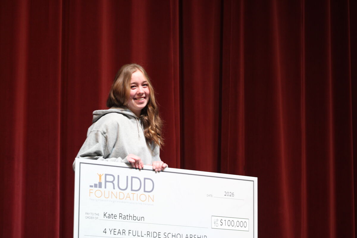 A smiling young woman holds a large check from the Rudd Foundation for a $100,000 scholarship.
