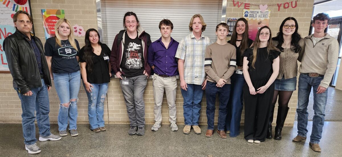 A group of ten people, including adults and young adults, stand together in a hallway.