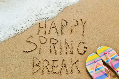 The words 'Happy Spring Break' are written in the sand, with a gentle wave approaching.