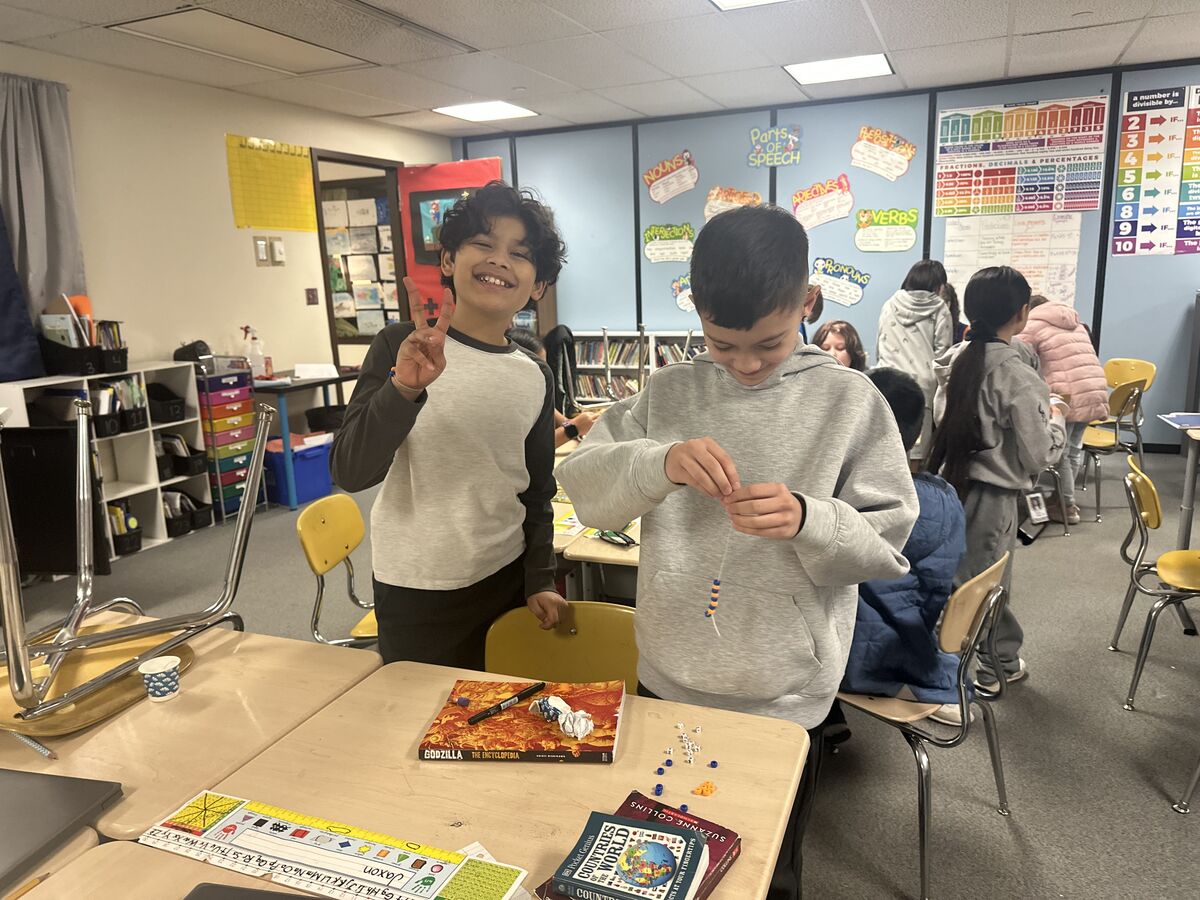 Two boys are engaged in a craft activity, stringing beads in a classroom.