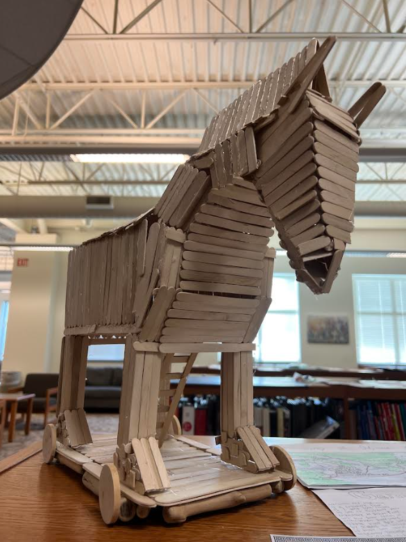 A detailed model of the Trojan Horse, constructed from popsicle sticks, sits on a wooden table.