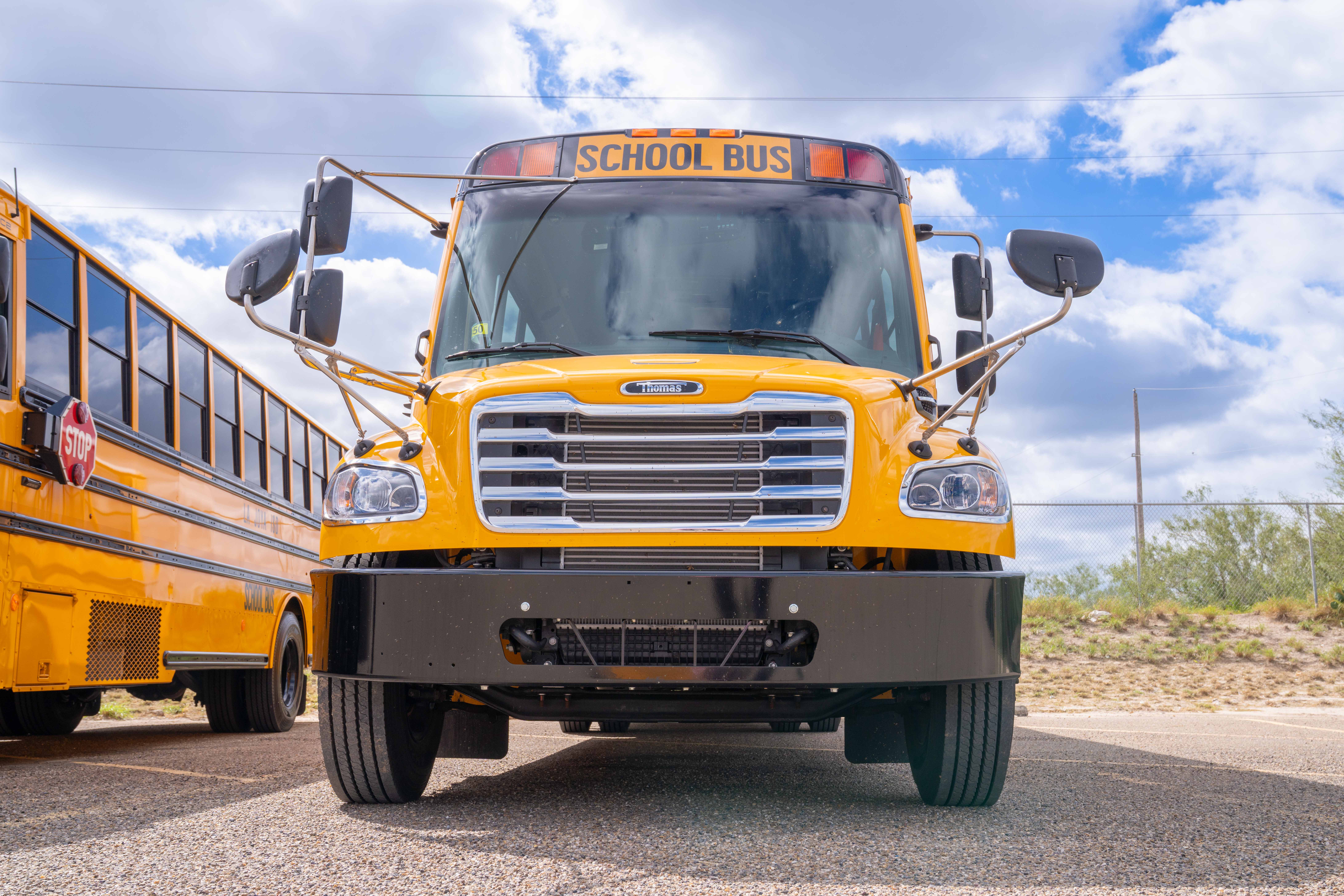 A bright yellow school bus parked outdoors under a partly cloudy blue sky, viewed from the front.