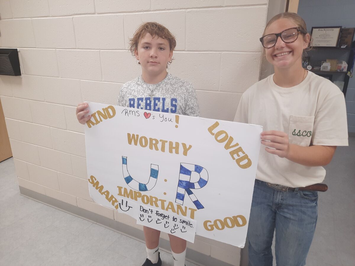 Two students hold a poster with positive messages in a school hallway.