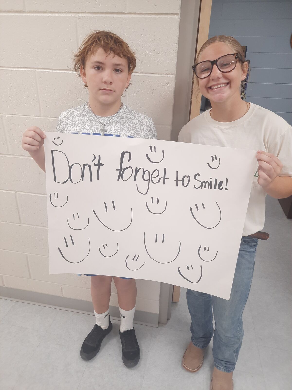Two people hold a white sign that says "Don't forget to Smile!" surrounded by hand-drawn smiley faces.