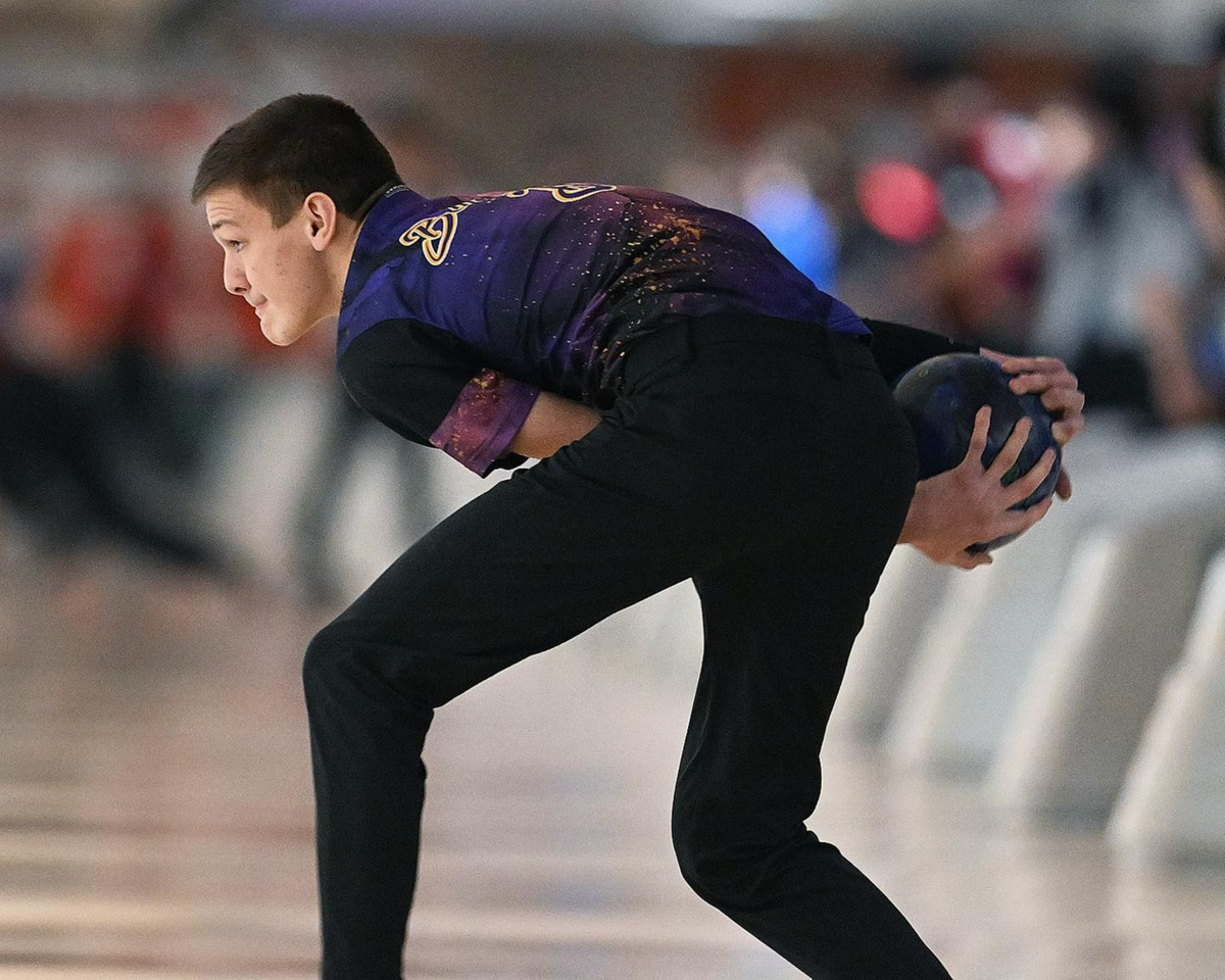 A bowling holds the ball with two hands and he approaches the lane
