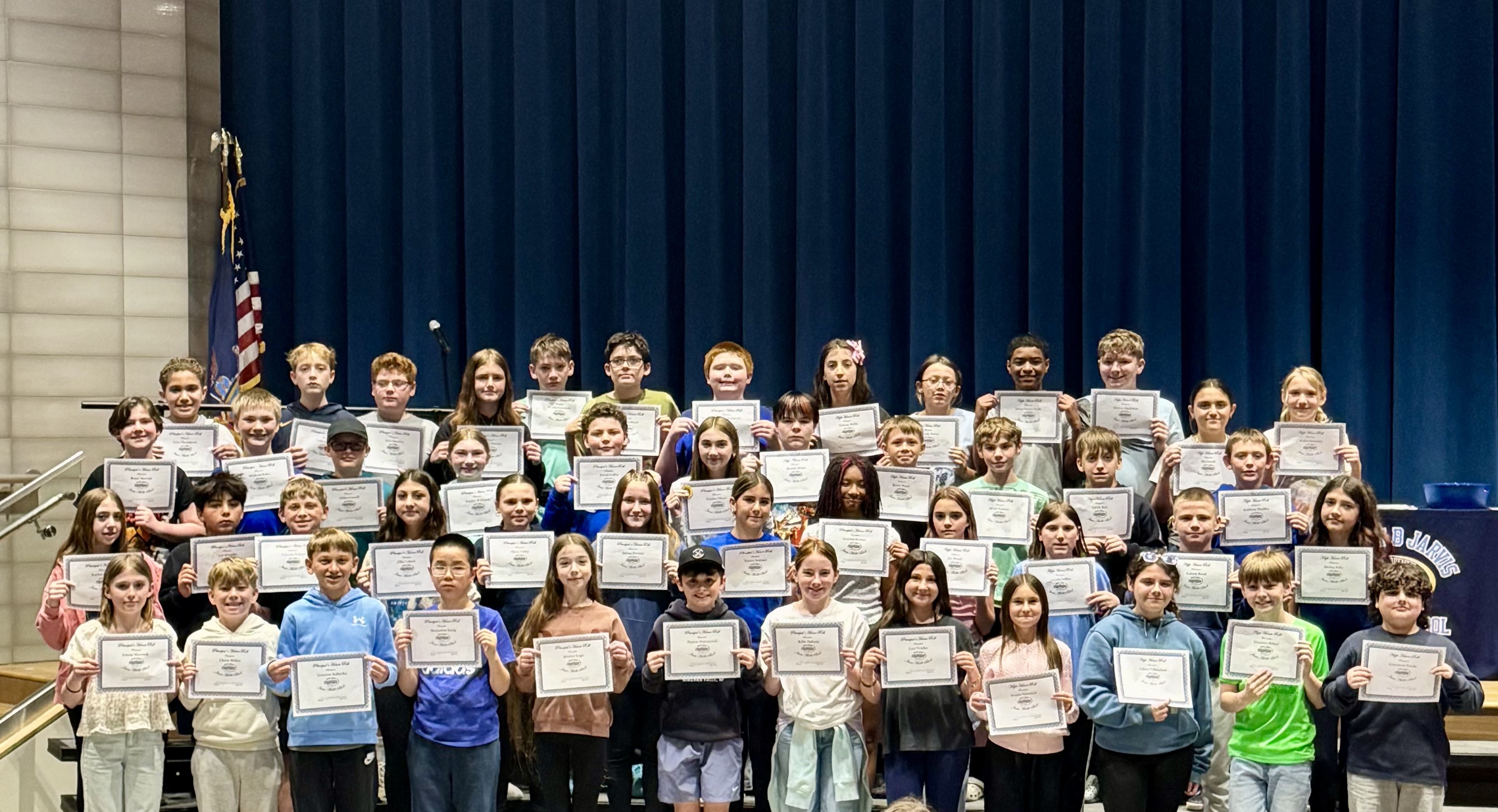 A large group of students stand on risers, proudly holding certificates.