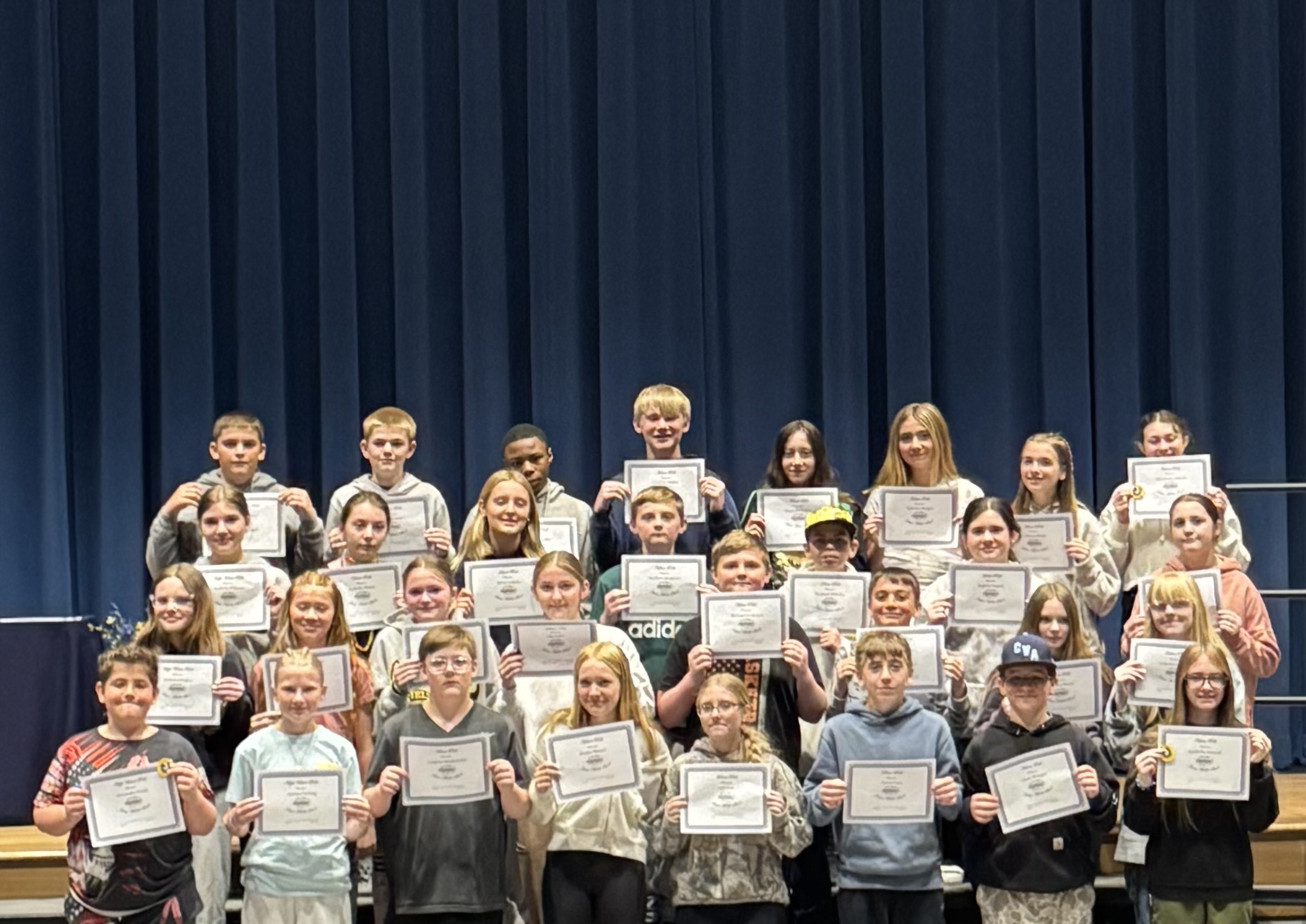 A group of students stand on a stage, holding certificates and smiling.