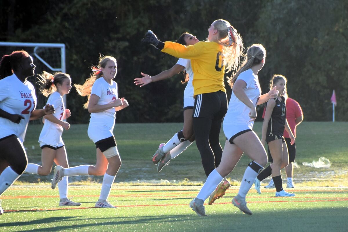 A goalkeeper in a yellow jersey jumps to make a save during an outdoor soccer game.