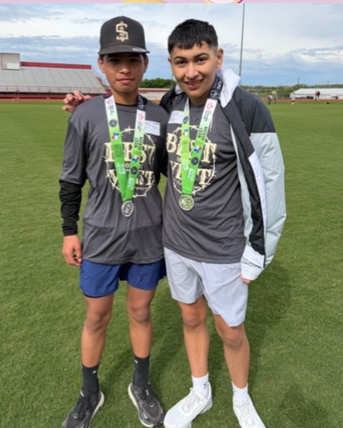 Two young athletes stand on a grassy field, proudly displaying their medals.
