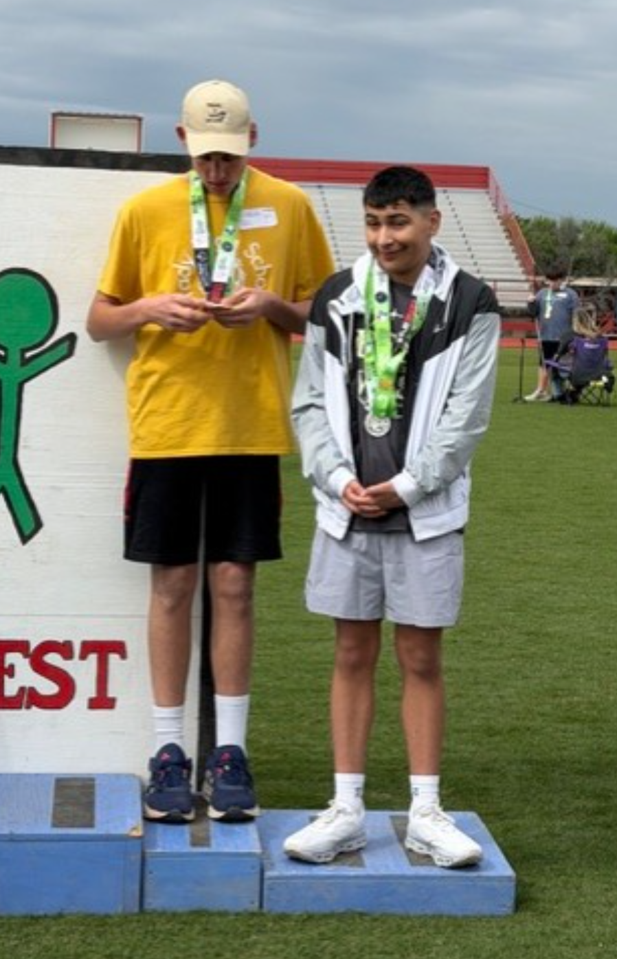 Two young athletes stand on a blue podium, wearing medals around their necks.