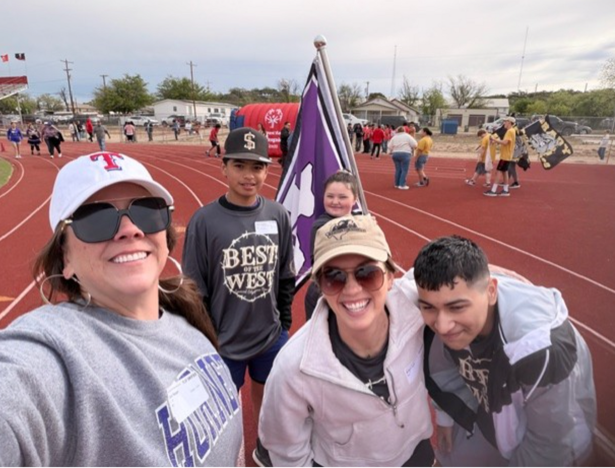 A group of people, including adults and youth, pose for a photo on a running track with a flag.