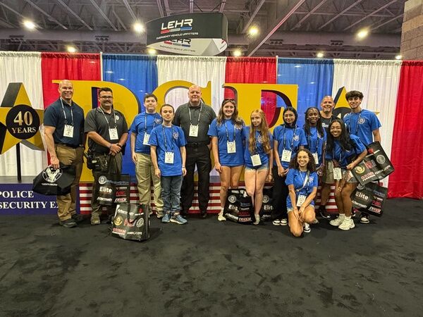 A group of adults and young people in blue shirts stand together in front of a backdrop with the letters "ADC" and "40 YEARS".