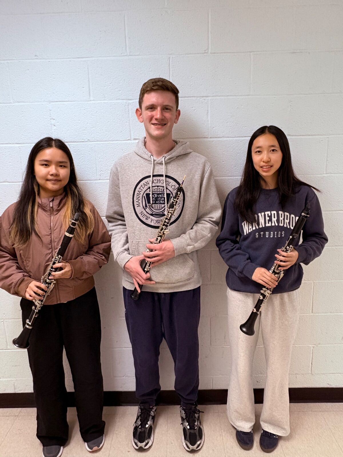 Three young musicians stand together, each holding a clarinet.