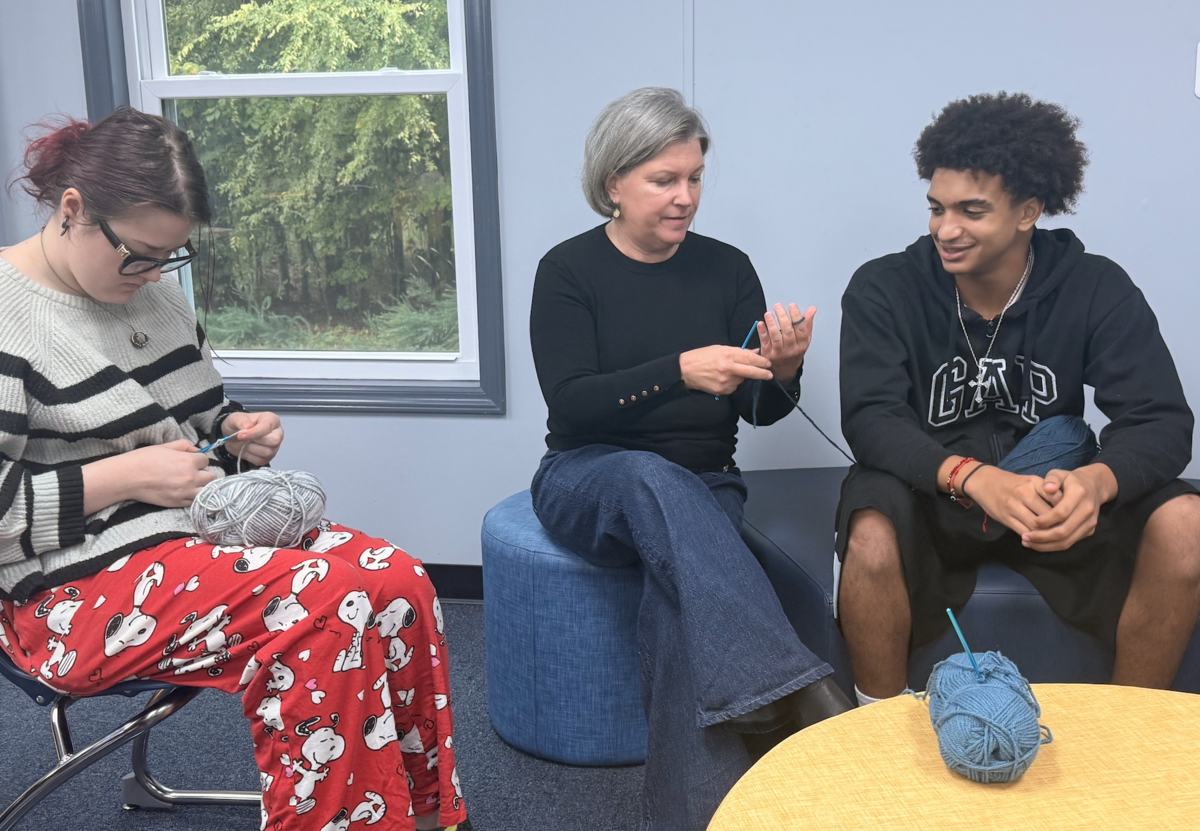 Three people sit together indoors, learning how to crochet yarn.