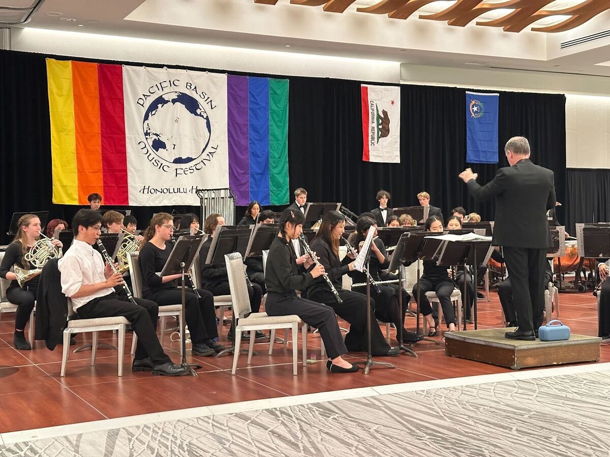 A conductor leads a diverse orchestra performing on a stage with colorful banners.