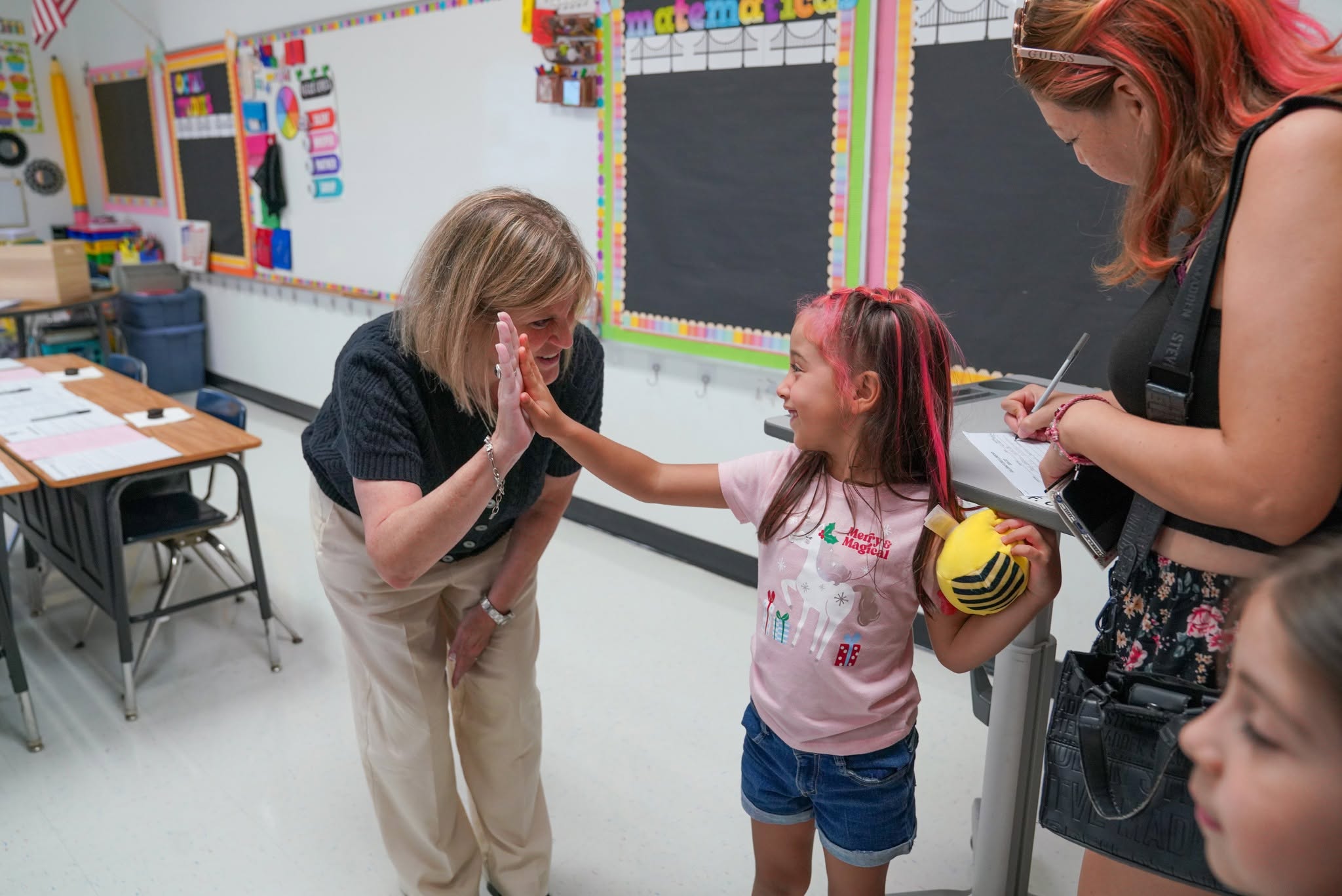 A teacher gives a young student a high-five in a colorful classroom.
