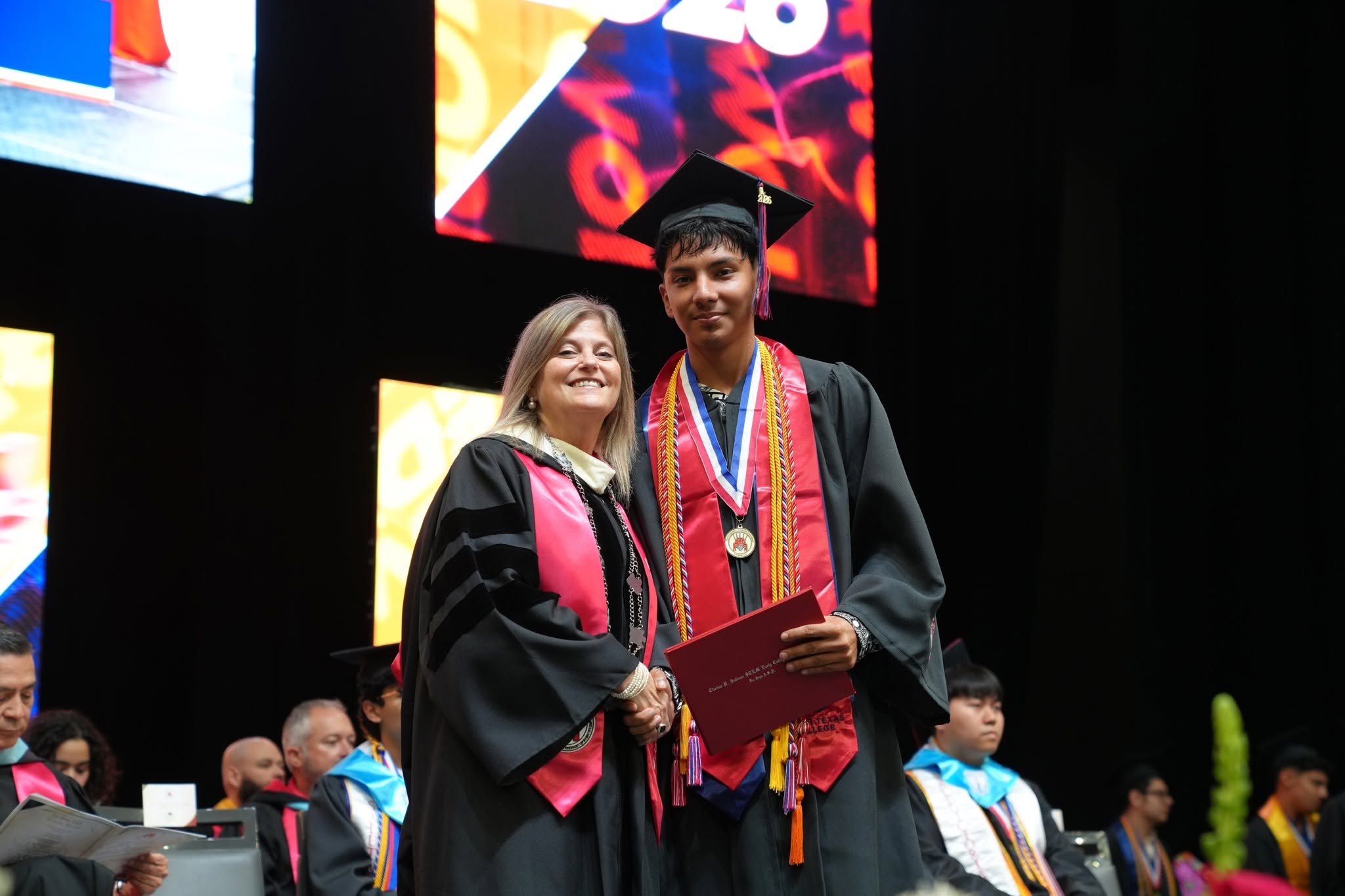 A graduate in a cap and gown receives a diploma from an official at a graduation ceremony.