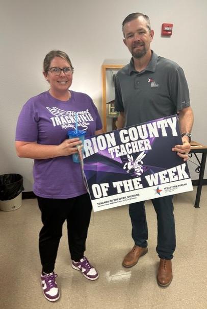 A woman in a purple 'Hornet Trackfield' shirt and a man in a grey polo shirt hold a sign that reads 'Marion County Teacher of the Week'.