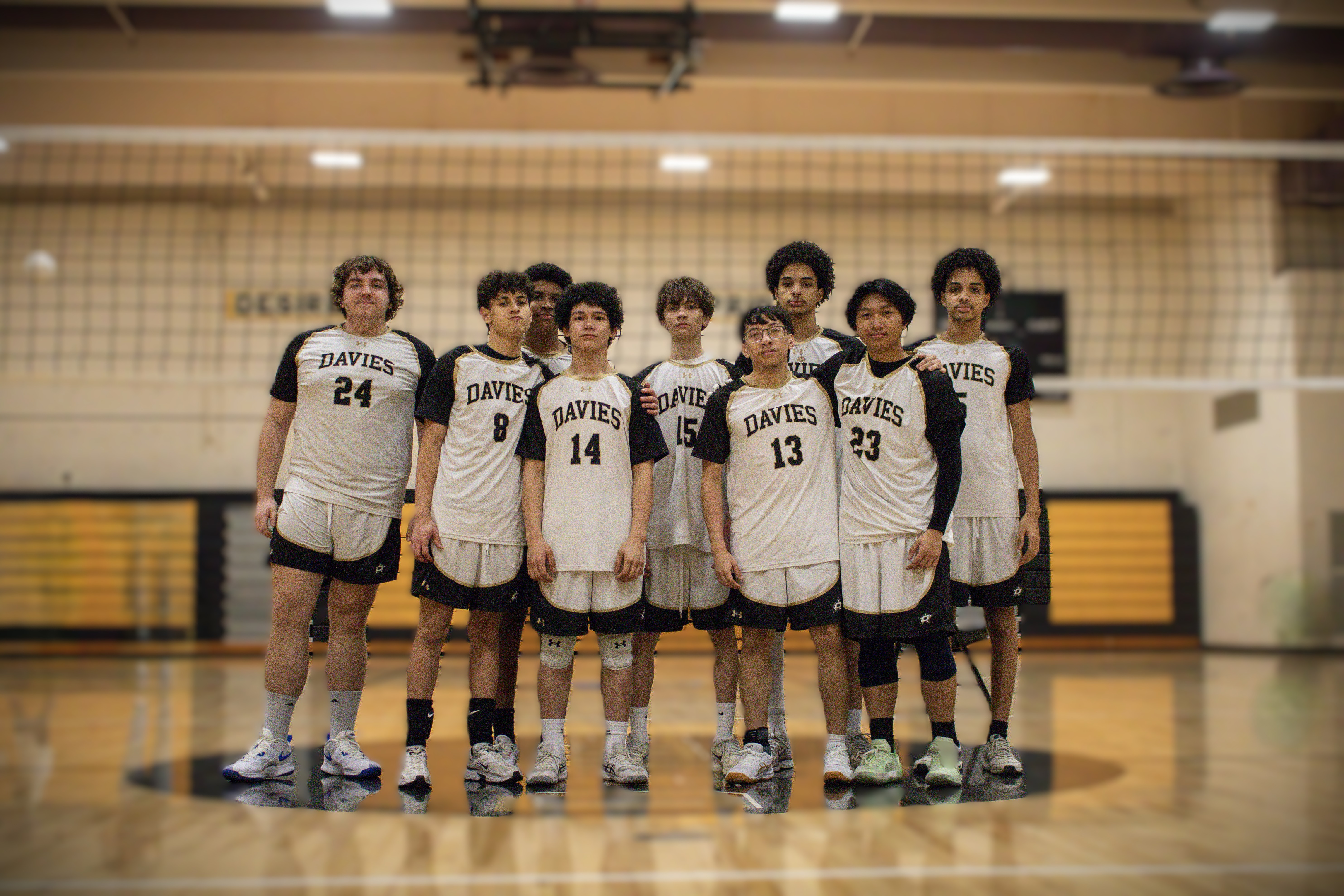 JV Boys Volleyball in matching volleyball uniforms stand together on a polished gym floor.