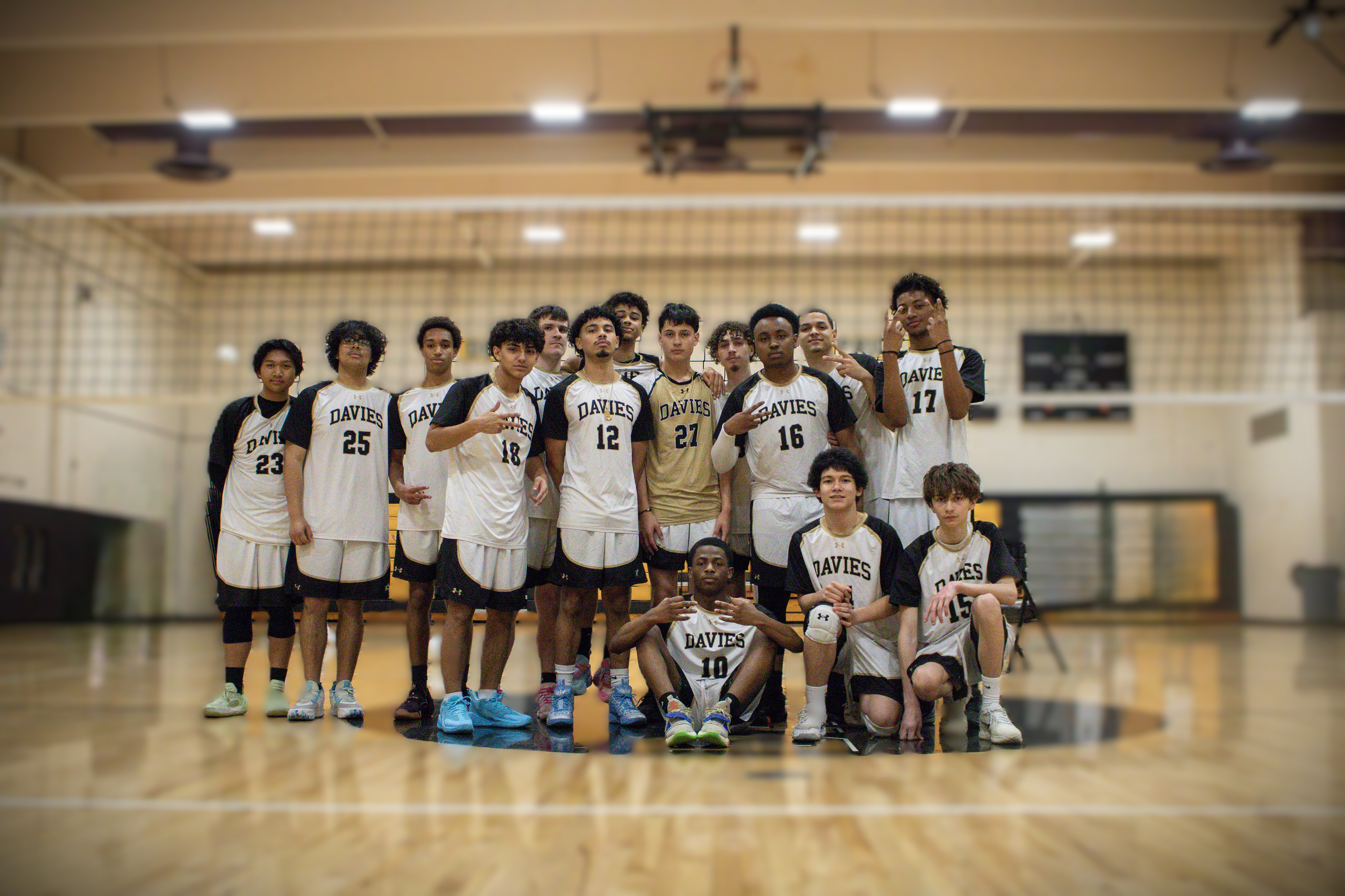 Davies' Boys Varsity Volleyball in matching white and black volleyball uniforms pose for a team photo on a wooden court.