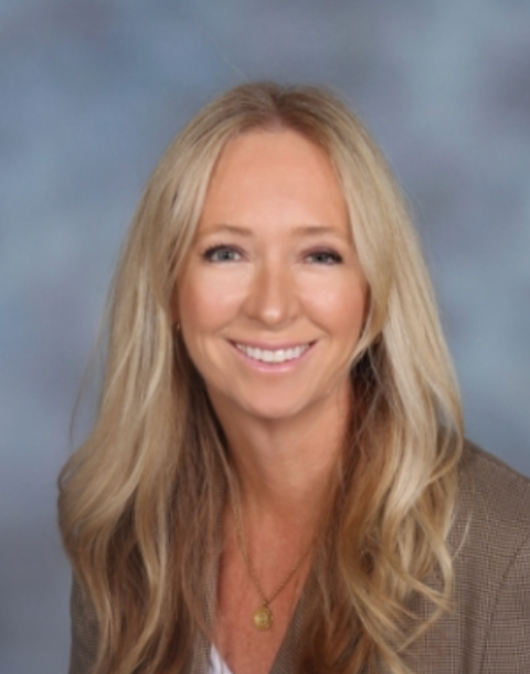 The new principal, A woman with blonde hair smiles warmly, wearing a brown blazer and a gold pendant necklace.