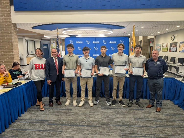 A group of students and adults stand together, holding certificates in a room with blue banners.