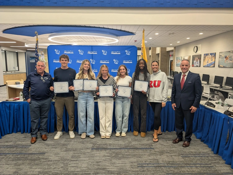 A group of students and adults stand together, holding certificates in a room with a blue backdrop.
