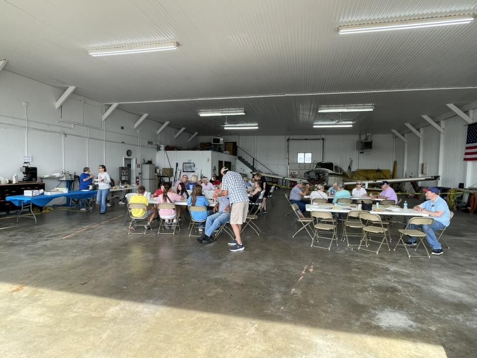 People gather for an event inside an airplane hangar, with tables set up for dining.