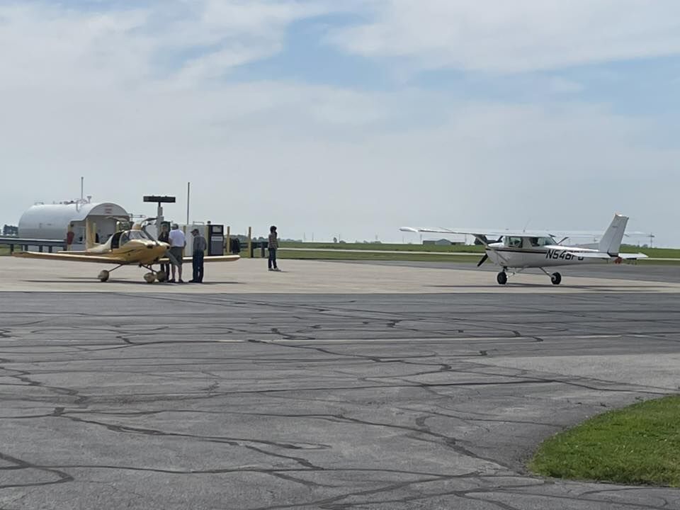 Two small airplanes are parked on an airport tarmac under a partly cloudy sky.