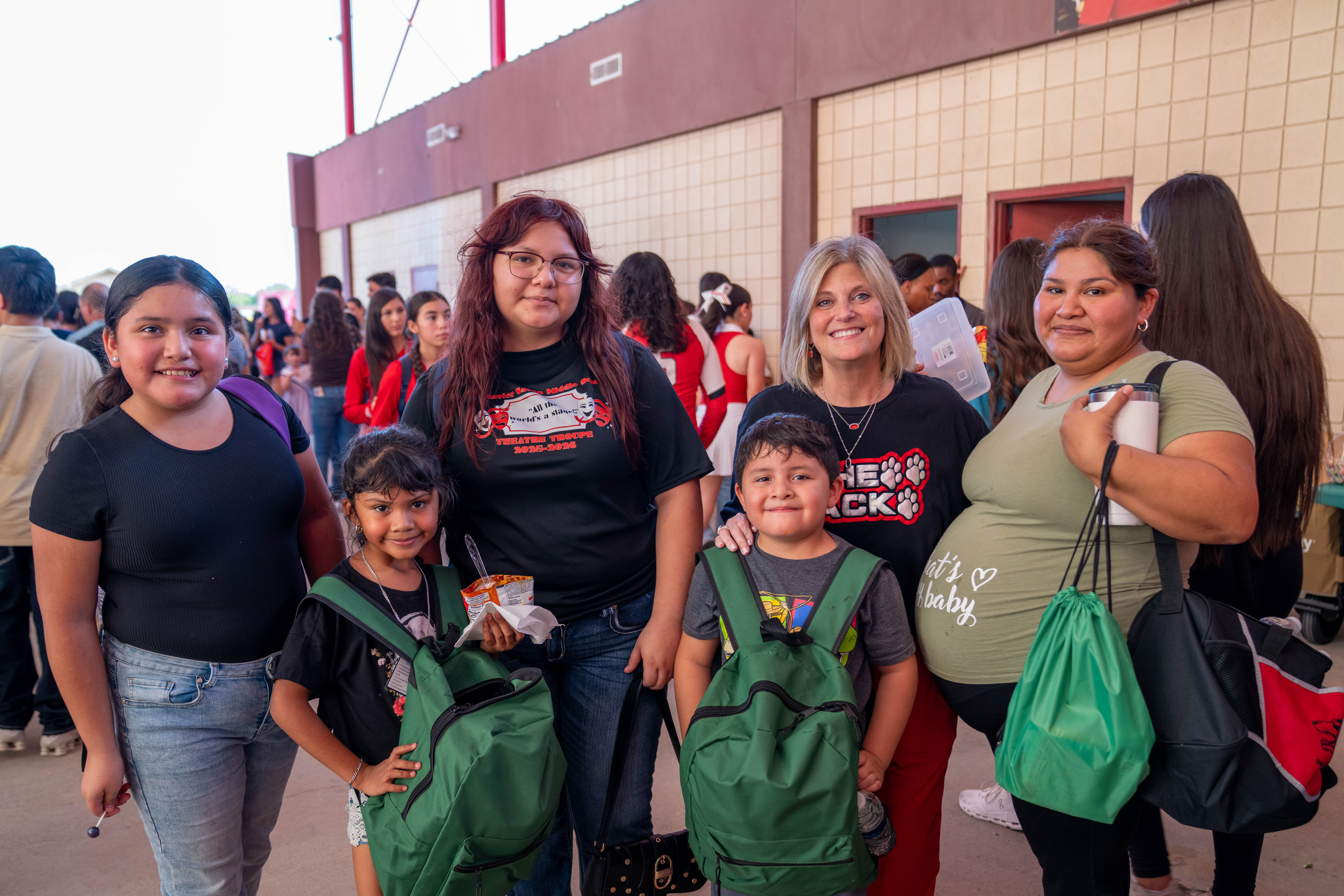 A group of women and children stand outdoors, smiling together near a brick building.