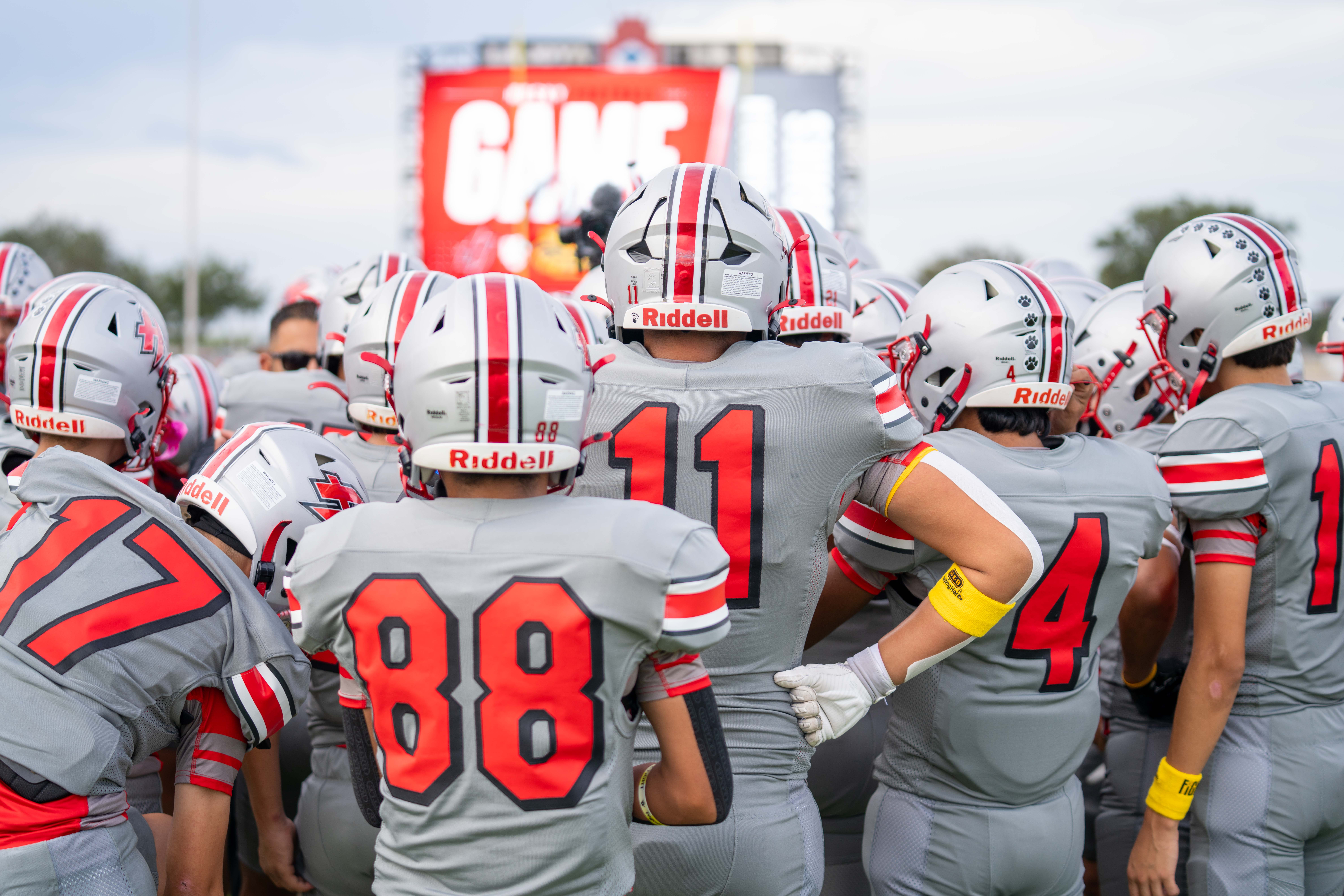 A rear view of a football team in grey and red uniforms huddled together on the field.