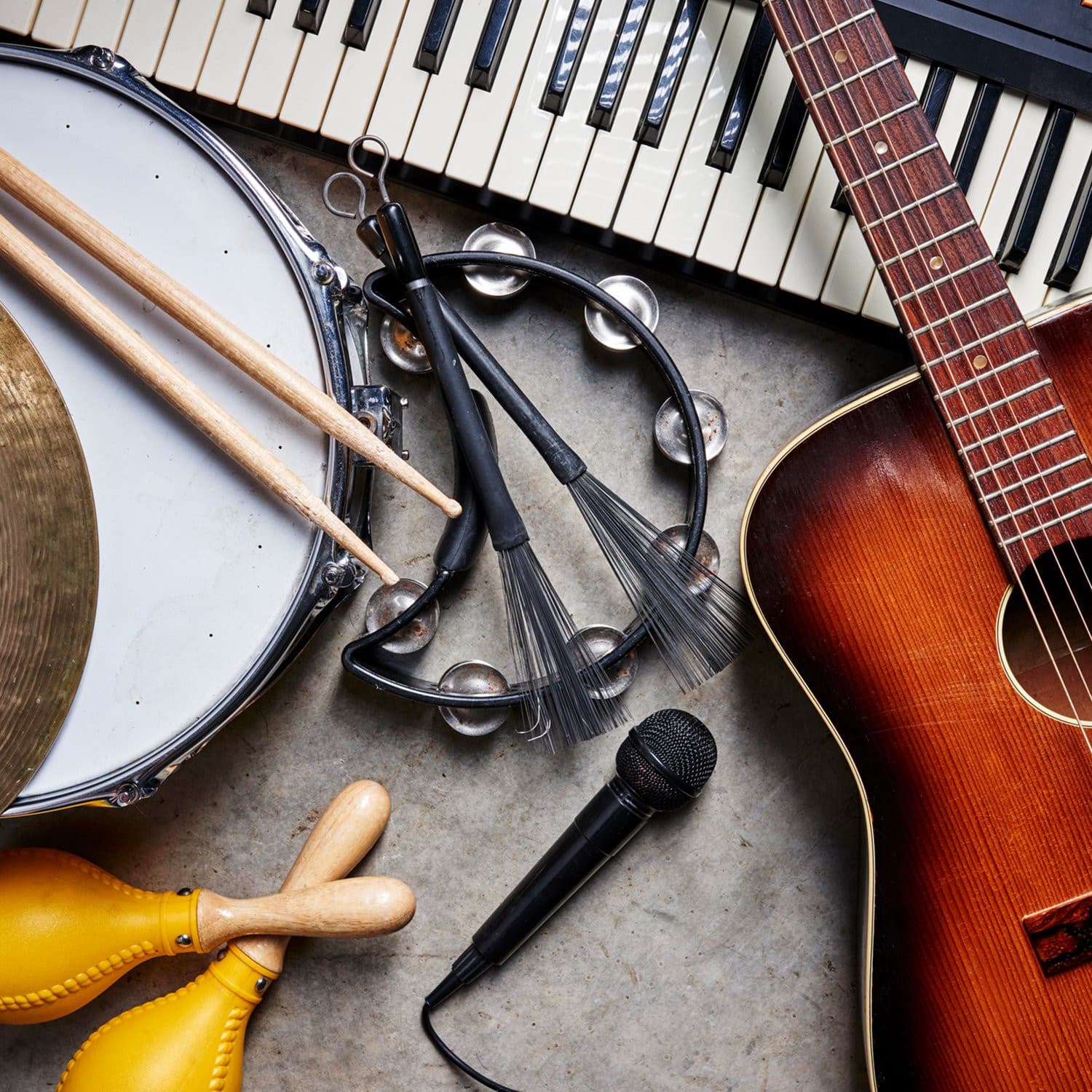 A collection of musical instruments including a guitar, keyboard, drum, and microphone are laid out on a concrete surface.