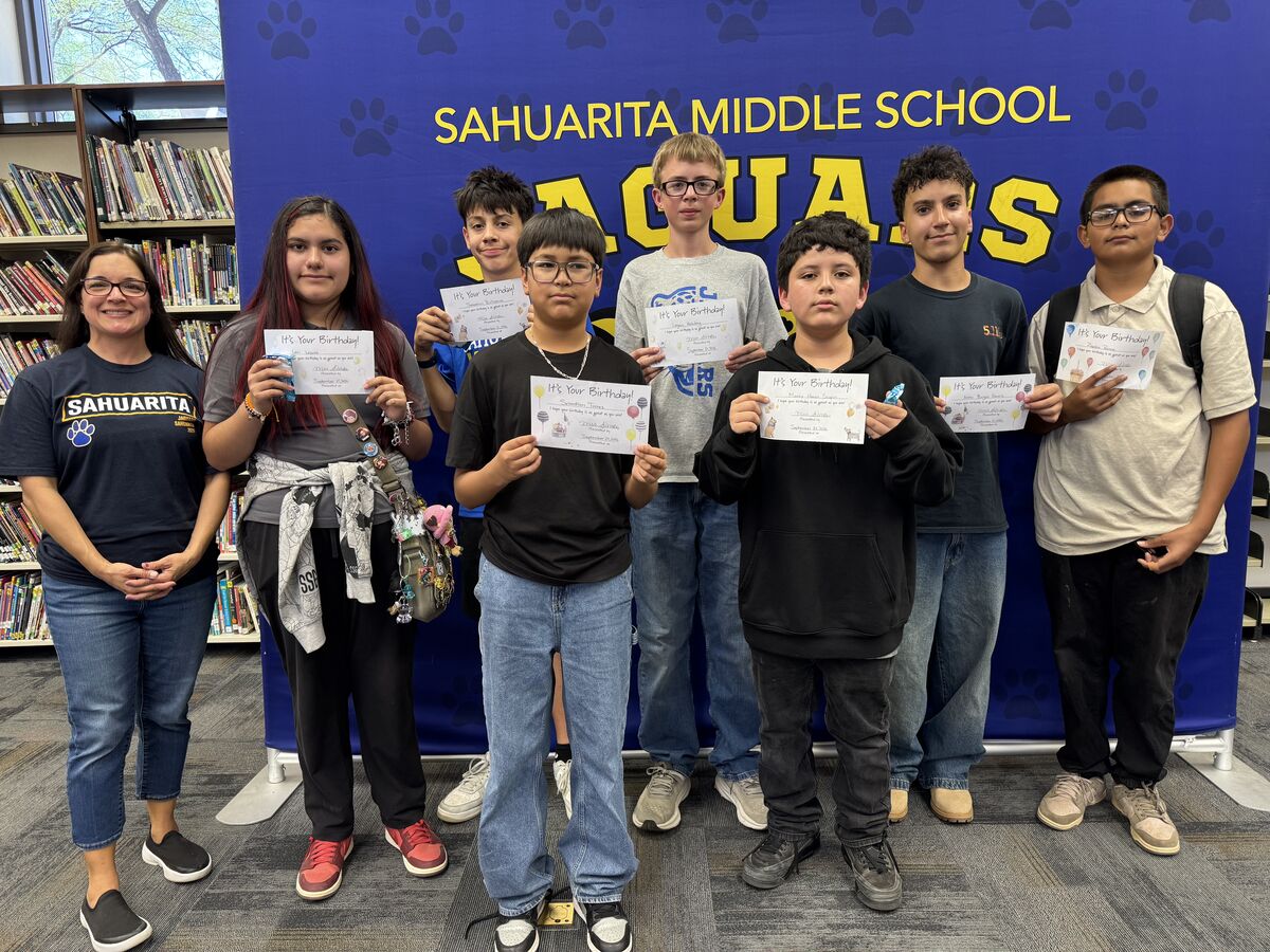 A group of students and an adult in front of a banner.