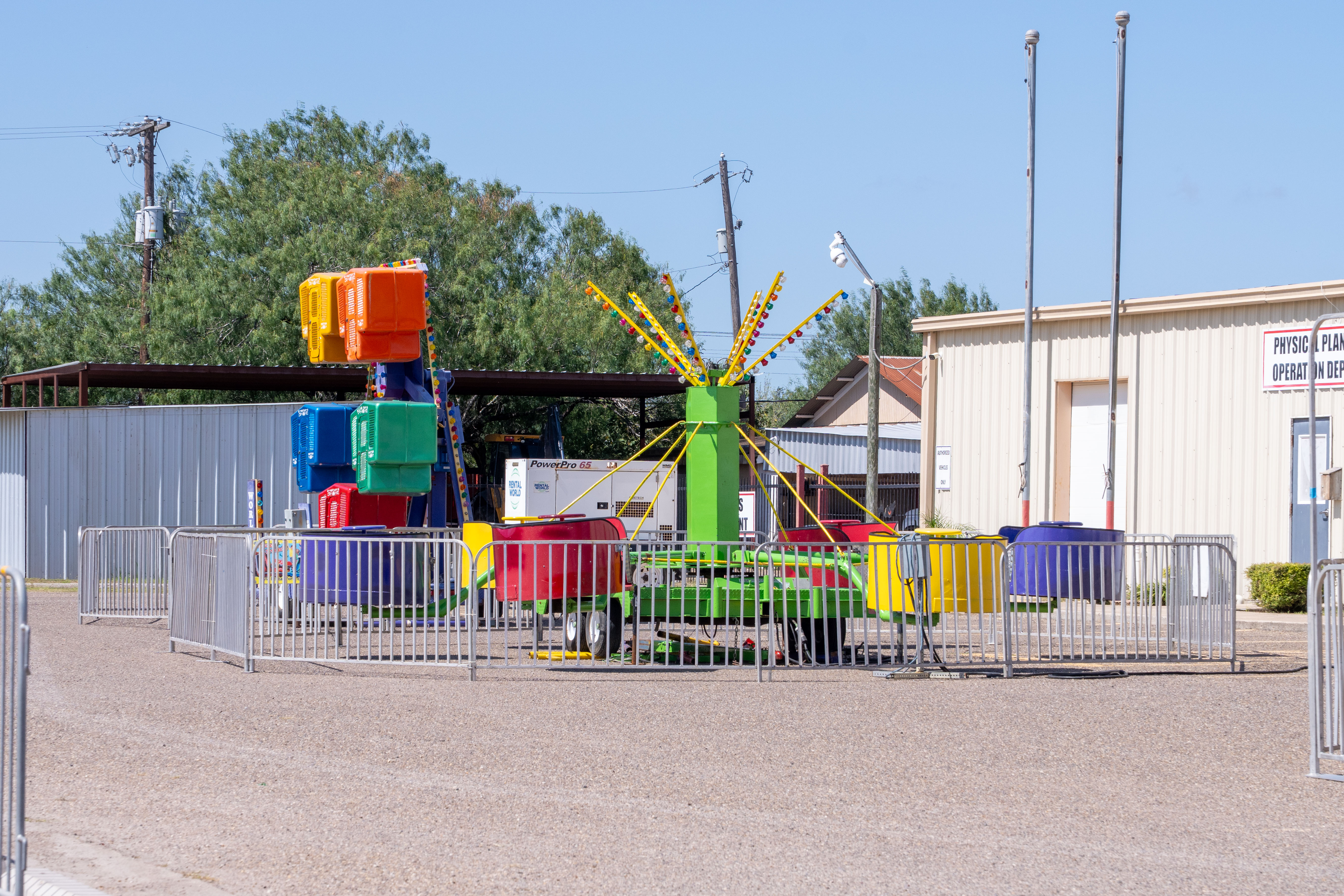 A colorful amusement park ride with yellow, orange, blue, and green pods sits on a paved lot.
