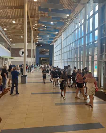A group of students walk through a bright, modern school hallway with large windows.