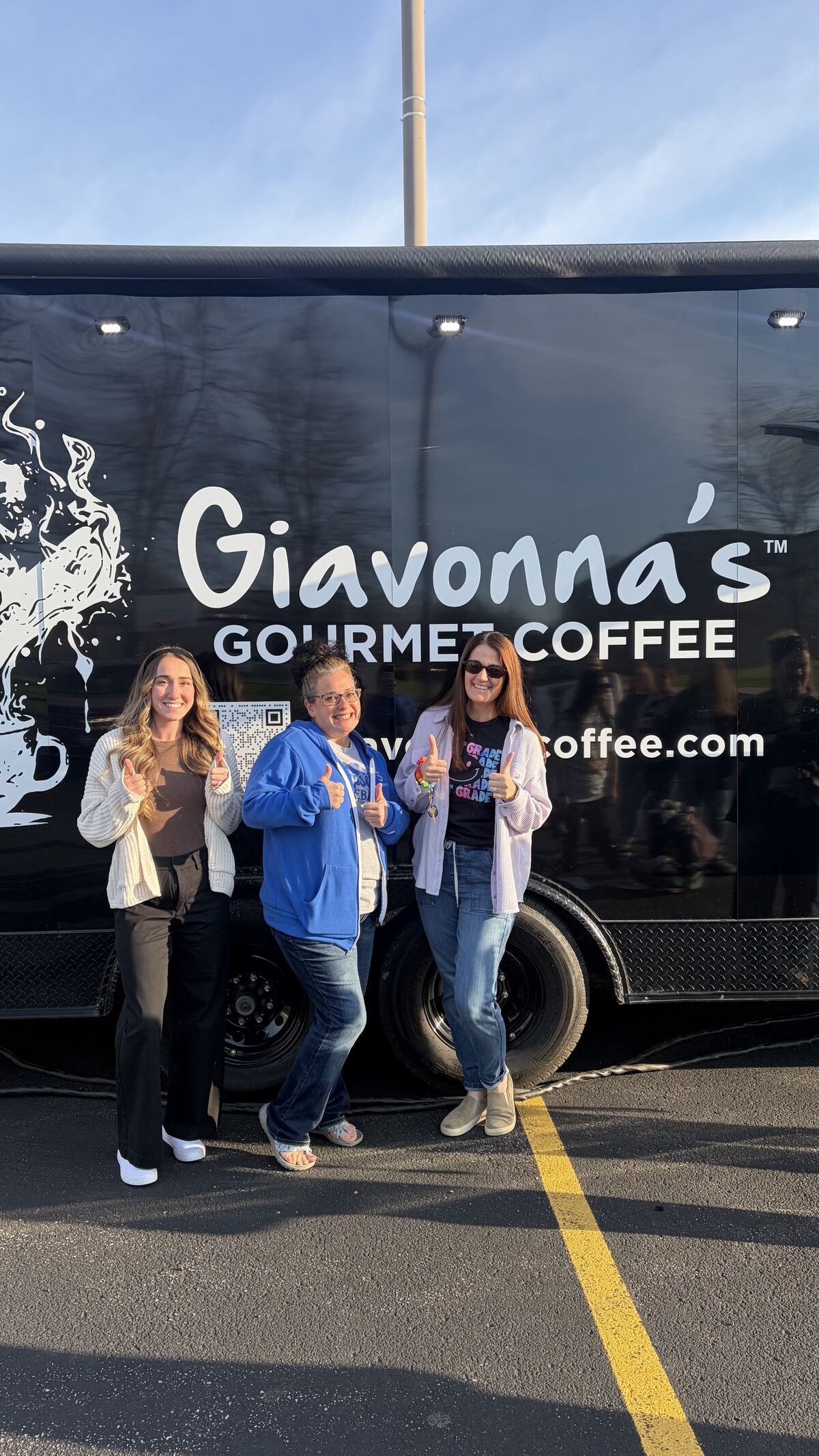 Three women give thumbs up in front of a black "Giavonna's Gourmet Coffee" food truck.