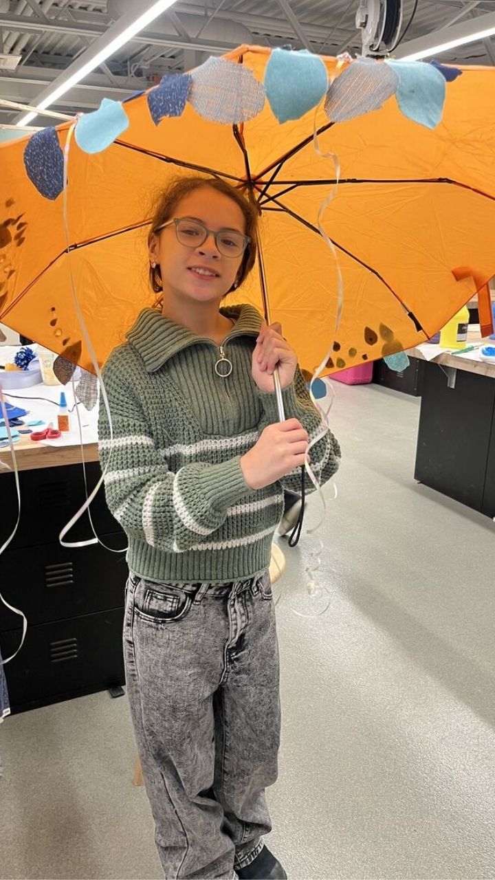 A young person smiles while holding a decorated orange umbrella with fabric circles attached.