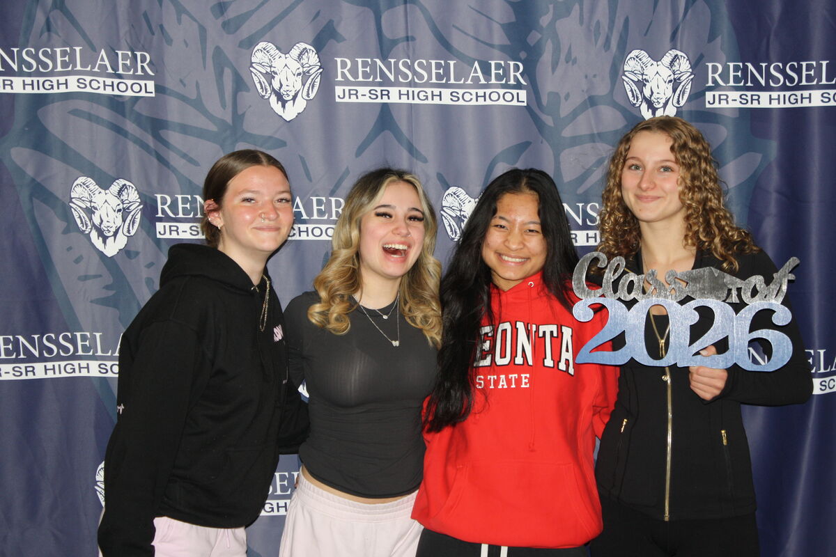 Four smiling young women pose for a photo in front of a Rensselaer Jr-Sr High School banner.