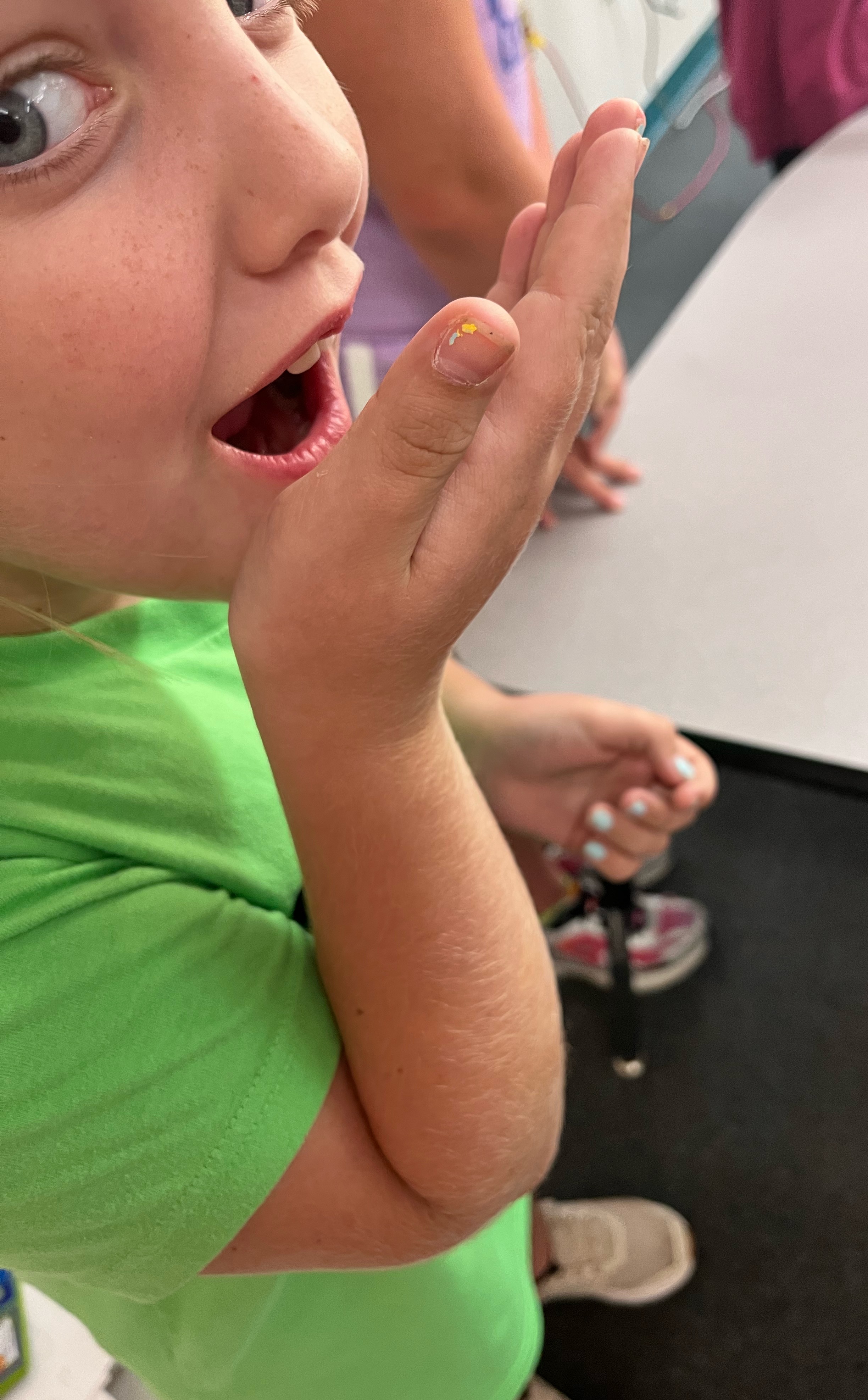 A close-up of a child in a bright green shirt cupping their hand to their mouth.