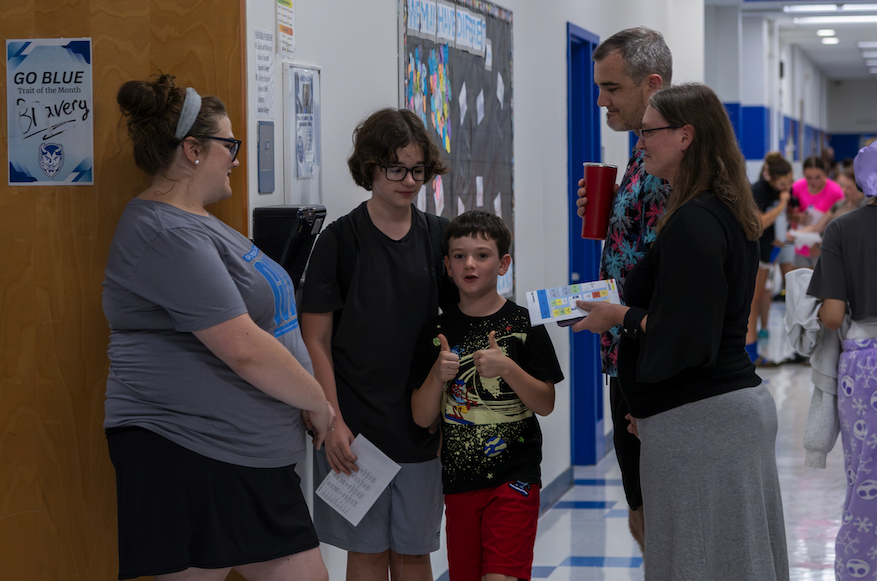 A group of adults and children converse in a school hallway.