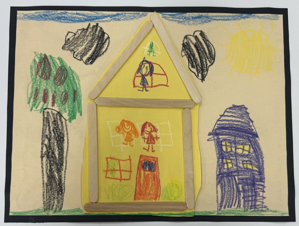 Drawing of a yellow house next to a tree. Underneath black clouds. Next to a smaller blue house. A family can be seen inside the yellow house.