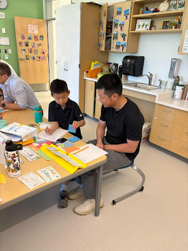 Parents sit with children in the classroom reviewing their school work. 