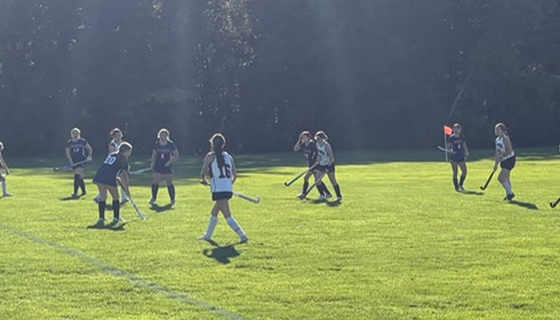 A group of youth field hockey players practice on a sunny grassy field.