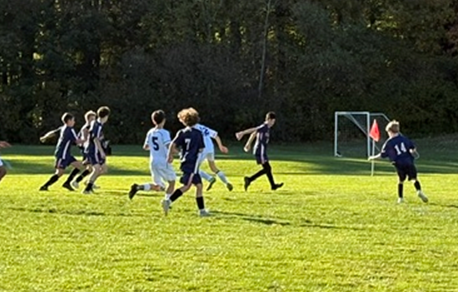 A group of youth soccer players run across a sunny green field during a game.