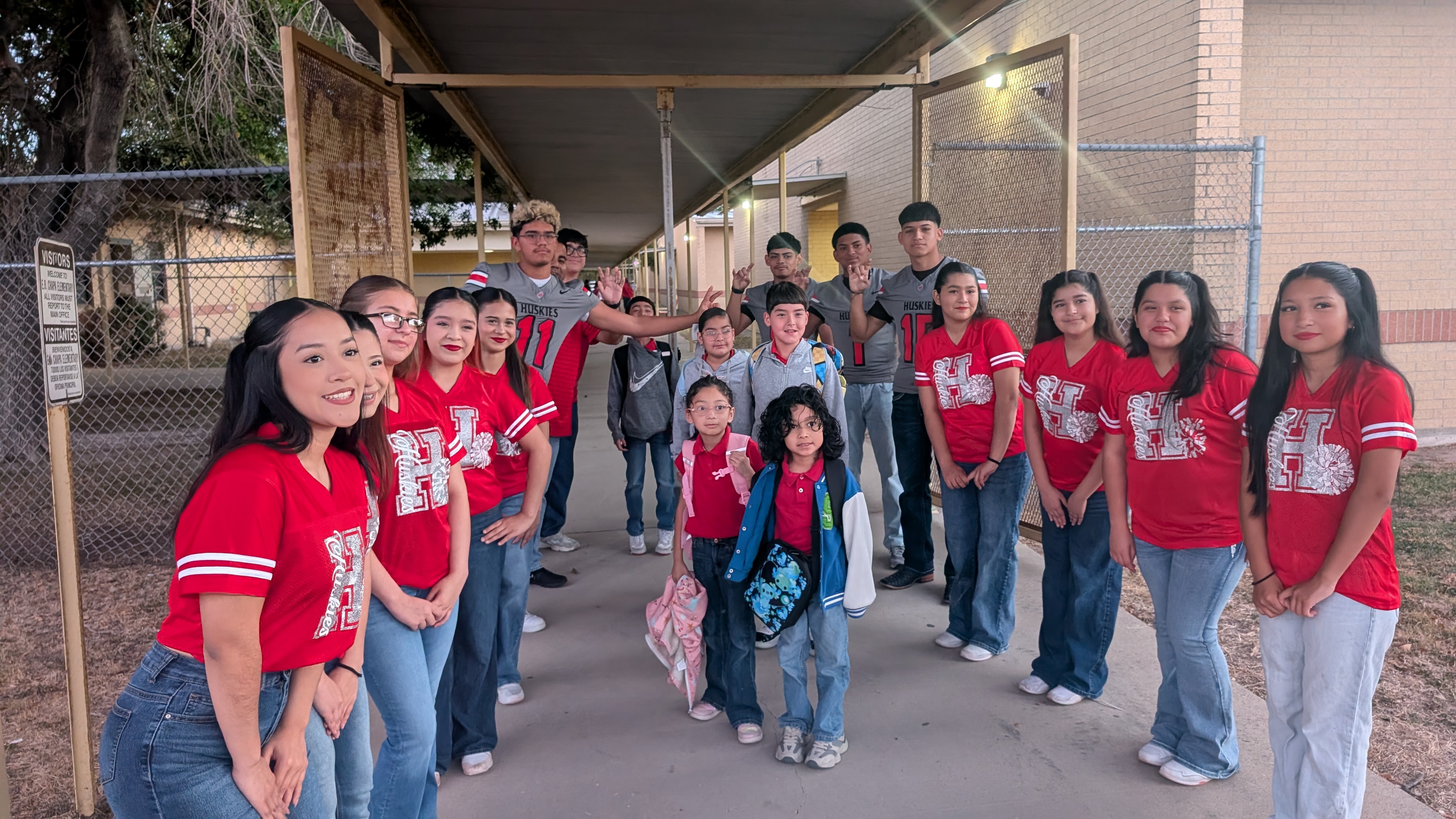 A large group of students in red shirts pose together outside a school building.