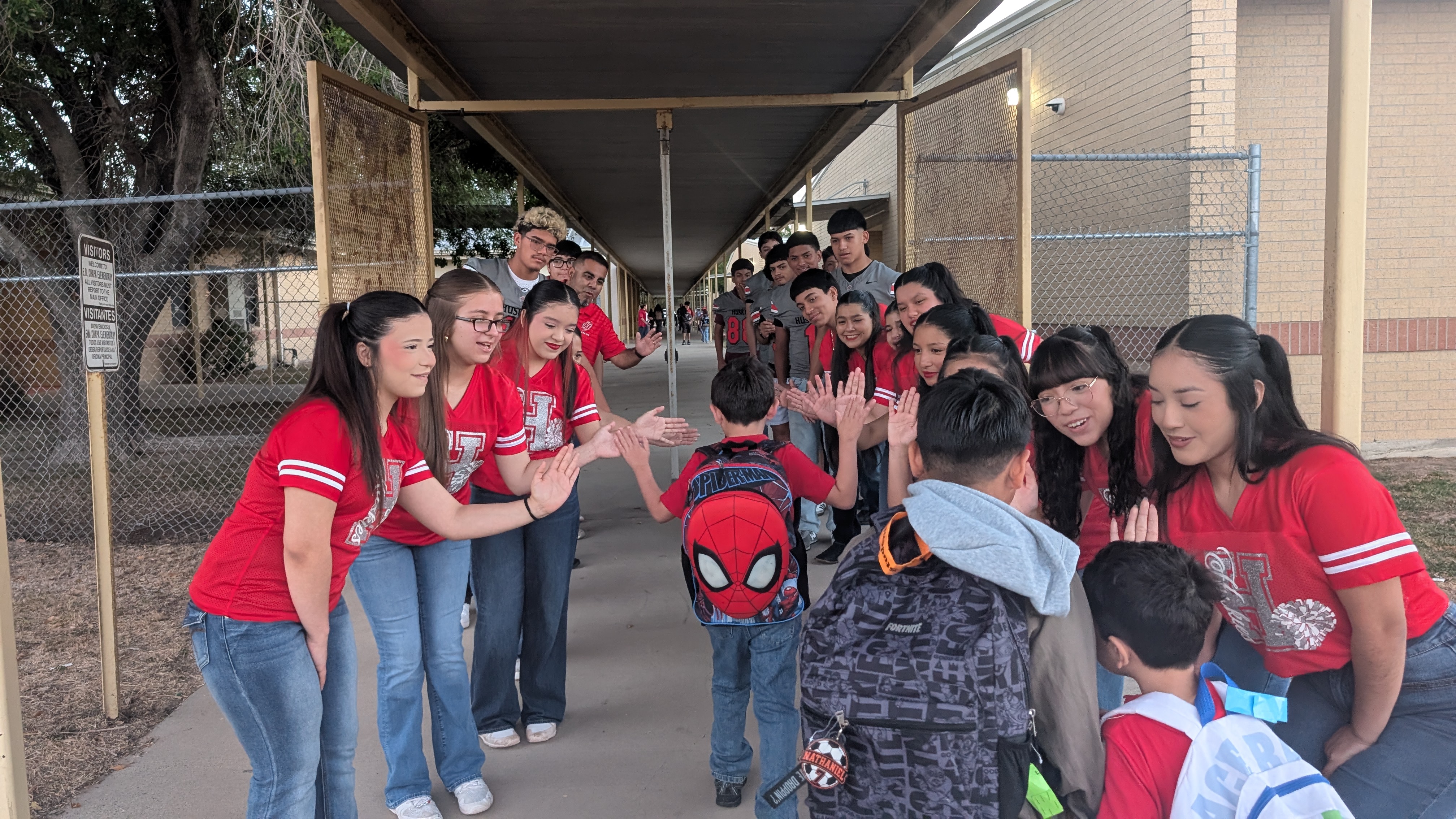 A group of students in red shirts create a tunnel of high-fives for younger children.