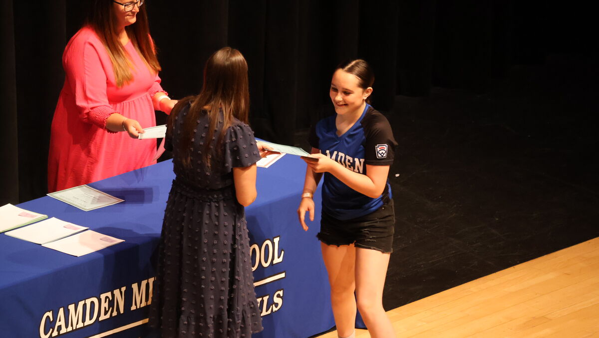 A student collects a certificate on stage from Mrs. DerCola