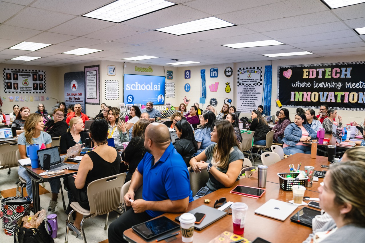 A diverse group of adults are seated at tables in a classroom, attending a presentation or workshop.